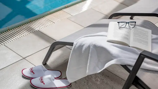 Poolside lounger with bathrobe, hotel slippers, book and glasses