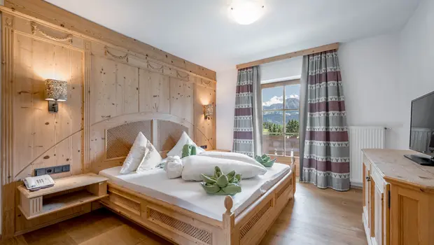 Alpin eingerichtetes Schlafzimmer mit Holzbett und Blick auf Wald und Berge