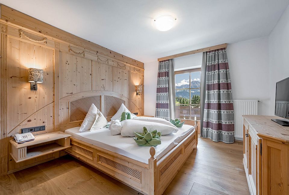 Alpin eingerichtetes Schlafzimmer mit Holzbett und Blick auf Wald und Berge