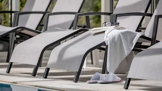 Wellnessliege mit Buch, Brille, Handtuch und Slipper am Poolrand