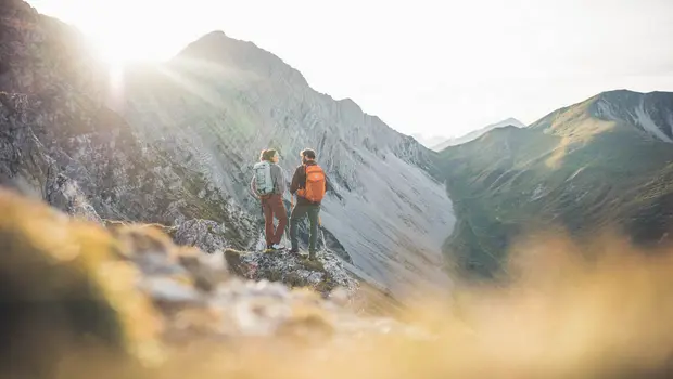 Wanderpaar genießt Bergblick in der Abendsonne auf felsigem Aussichtspunkt