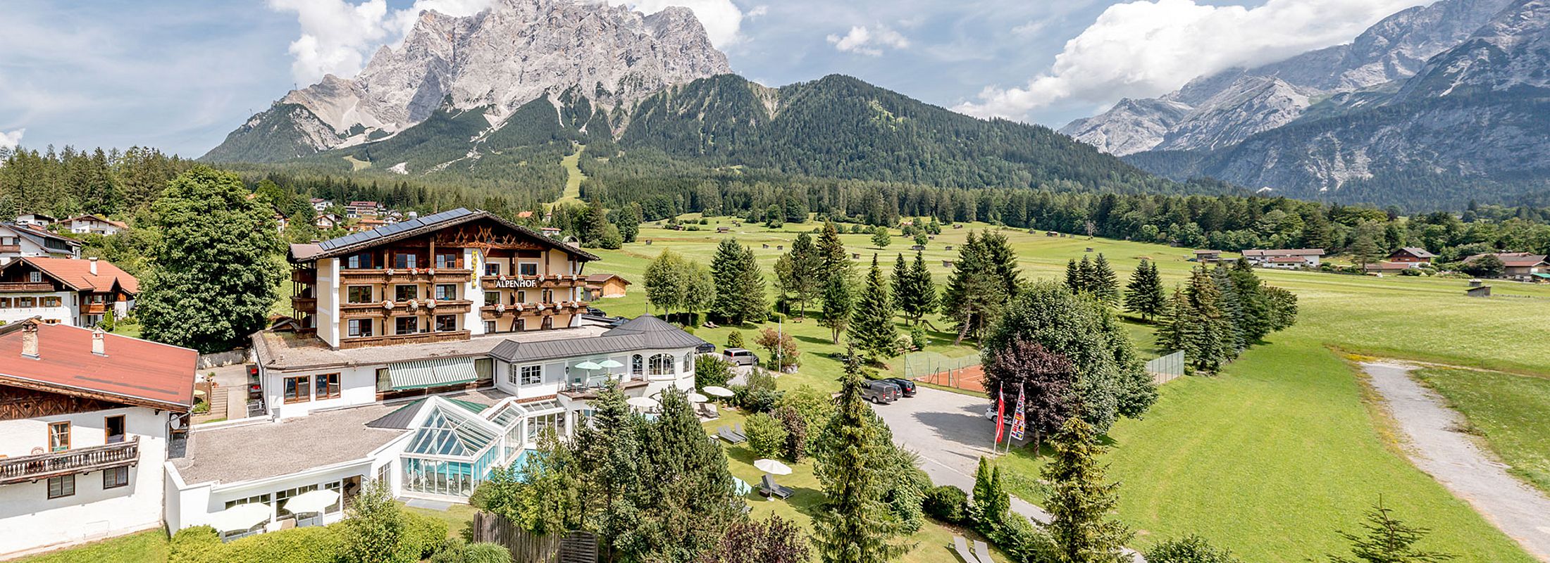 Alpenhof mit Liegewiese, Tennisplatz und Blick auf grüne Wälder und imposante Berggipfel